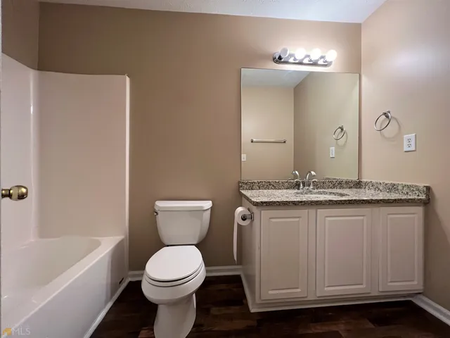a bathroom with a granite countertop toilet a sink a mirror and bathtub