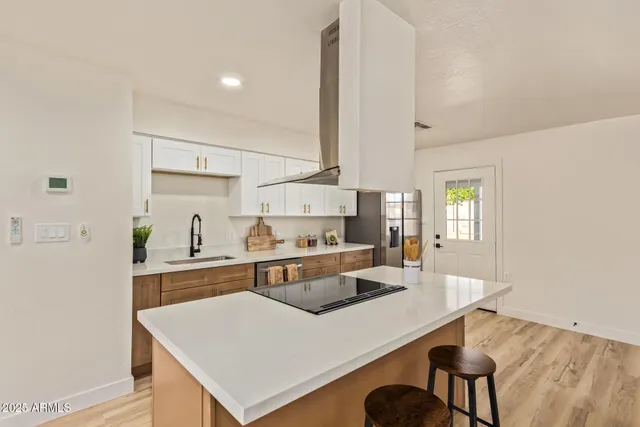 a large kitchen with kitchen island a stove a sink a refrigerator and white cabinets with wooden floor