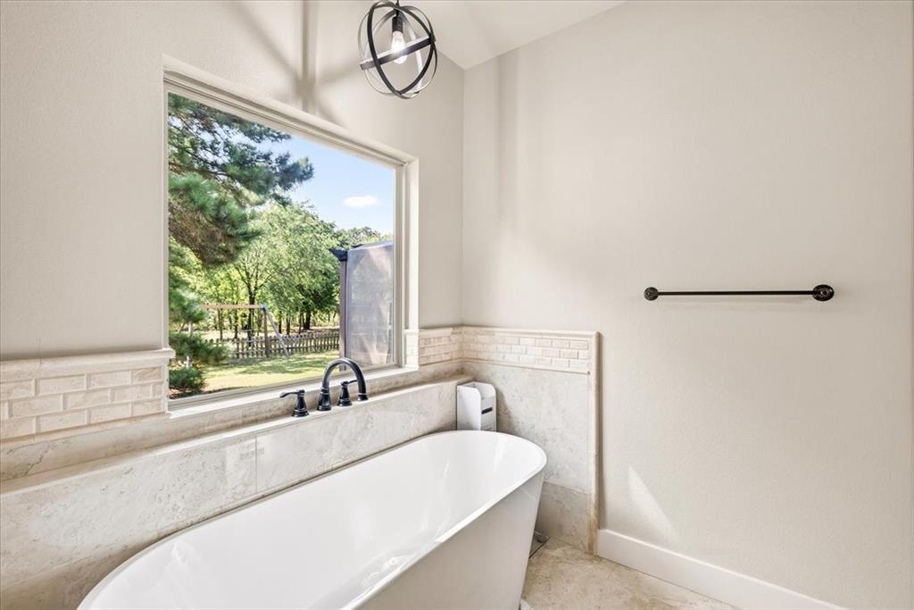 531 VZ County Road Eustace, TX 75124 - Photo 12 of 35 Freestanding soaking tub with matte black fixtures, framed window, beige subway tile detailing, and an industrial-style overhead light fixture