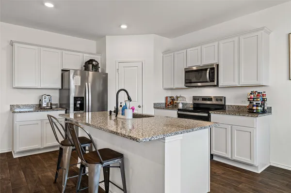 a kitchen with kitchen island granite countertop a stove top oven a sink a dining table and chairs with wooden floor