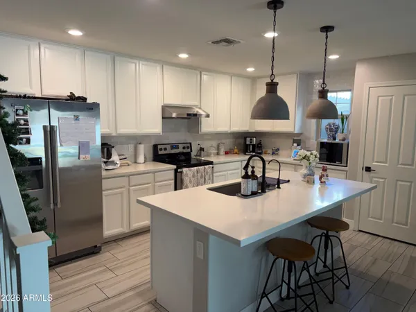 a kitchen with stainless steel appliances granite countertop a sink a stove a refrigerator and white cabinets with wooden floor