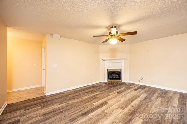 a view of an empty room with chandelier fan and wooden floor
