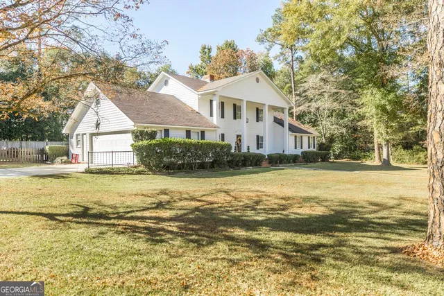 a view of a white house next to a yard with a large trees and a big yard