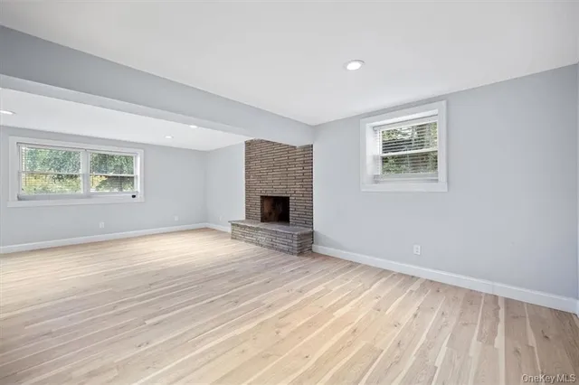 a view of an empty room with wooden floor fireplace and a window