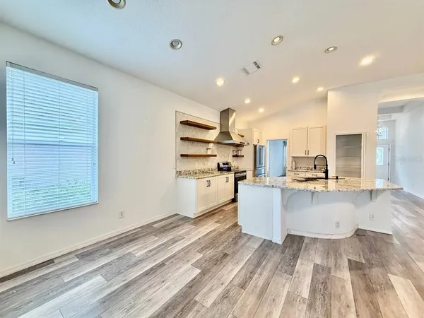 a large white kitchen with kitchen island a stove a sink dishwasher and white cabinets with wooden floor