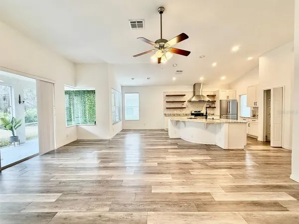 a view of an empty room and kitchen with wooden floor