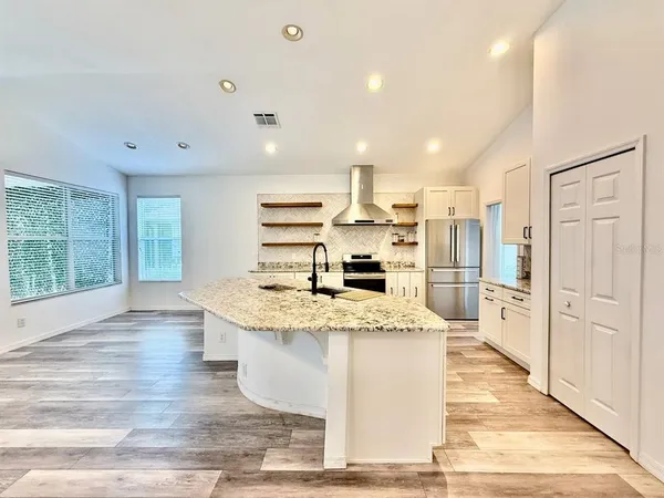 a large kitchen with stainless steel appliances kitchen island granite countertop a refrigerator a stove a sink and white cabinets with wooden floor