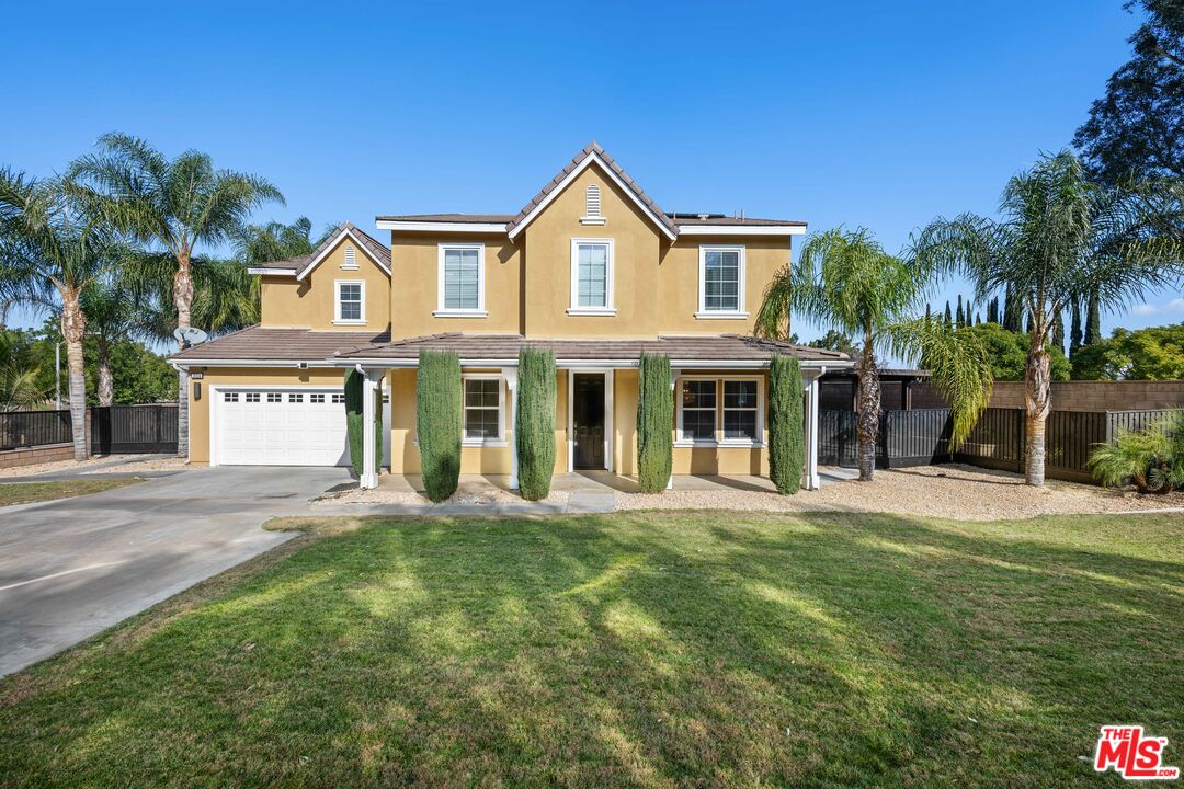 a view of a white house with a large windows and a yard with plants and palm trees
