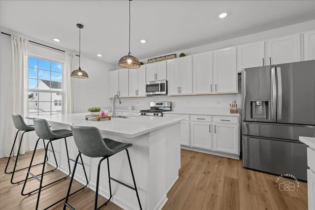 a kitchen with stainless steel appliances white cabinets a sink a stove a refrigerator and island with wooden floor