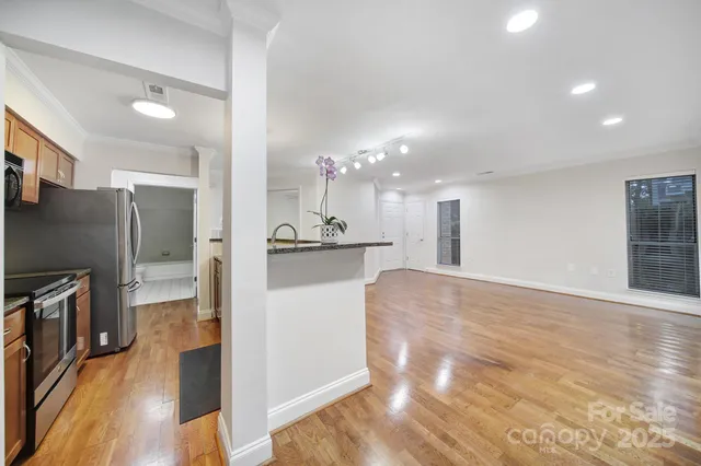 a kitchen with stainless steel appliances granite countertop a refrigerator a sink dishwasher a oven and white cabinets with wooden floor