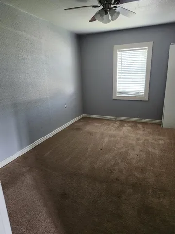 an empty room with a chandelier fan and windows