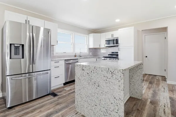 a kitchen with stainless steel appliances granite countertop a refrigerator a stove a sink and white cabinets with wooden floor