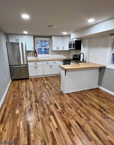 a kitchen with stainless steel appliances granite countertop a sink dishwasher a refrigerator and white cabinets with wooden floor