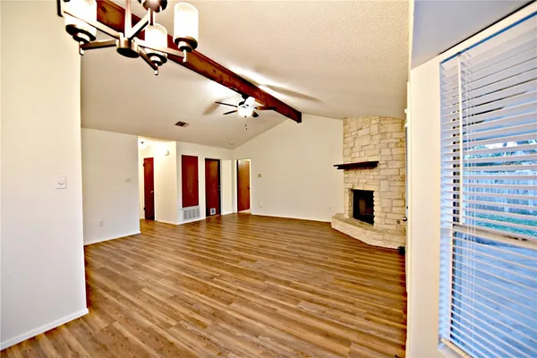 a view of an empty room with chandelier fan and wooden floor