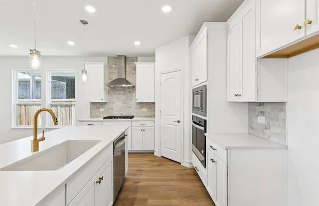 a large kitchen with stainless steel appliances kitchen island granite countertop a stove a sink a refrigerator and white cabinets with wooden floor