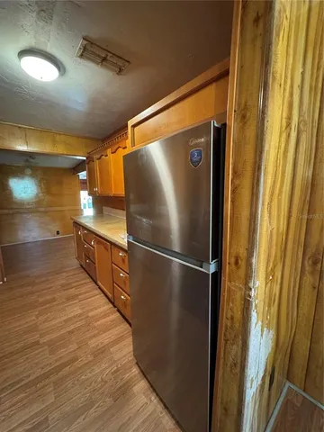 a view of a refrigerator in kitchen and an empty room with wooden floor
