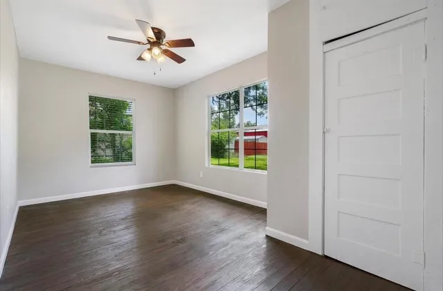 an empty room with wooden floor chandelier fan and windows