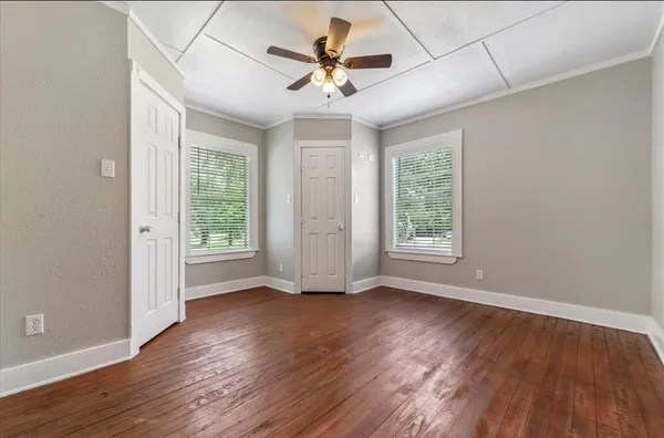 an empty room with wooden floor chandelier fan and windows
