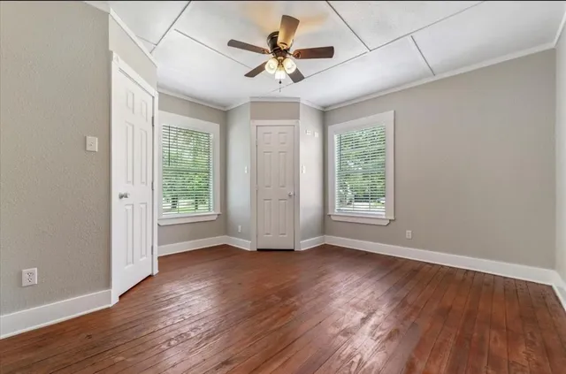 an empty room with wooden floor chandelier fan and windows