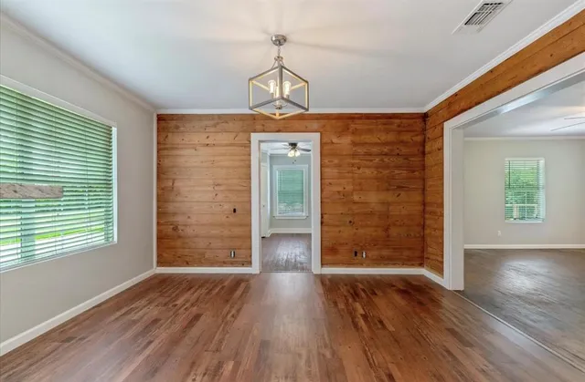 an empty room with wooden floor chandelier and windows