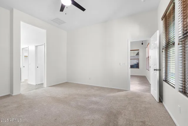 an empty room with chandelier fan and windows