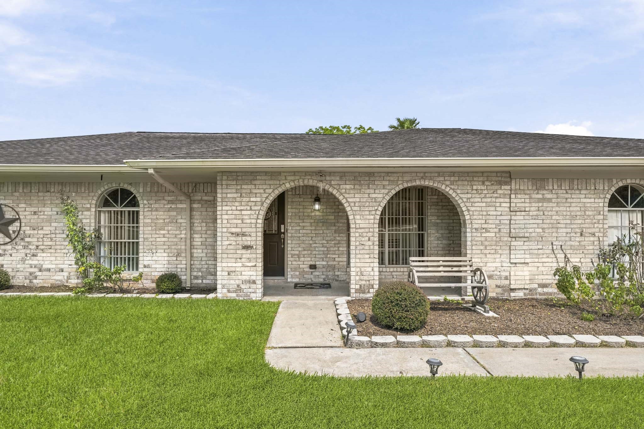302 Country Road 893 Angleton, TX 77515 - Photo 7 of 26 Chharming home with a brick exterior, featuring arched windows and a welcoming front porch. A well-maintained lawn and a cozy bench add to its curb appeal.
