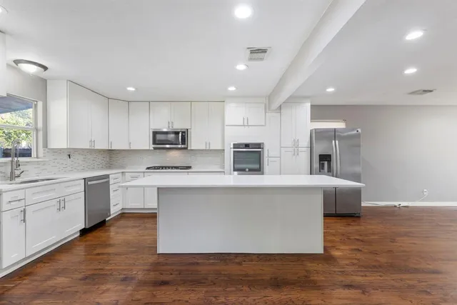 a large kitchen with stainless steel appliances granite countertop a large center island a sink a stove a refrigerator and cabinets