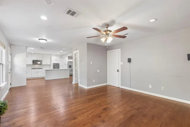 a view of an empty room with wooden floor and a kitchen