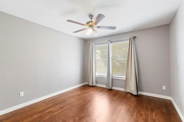 an empty room with wooden floor fan and windows
