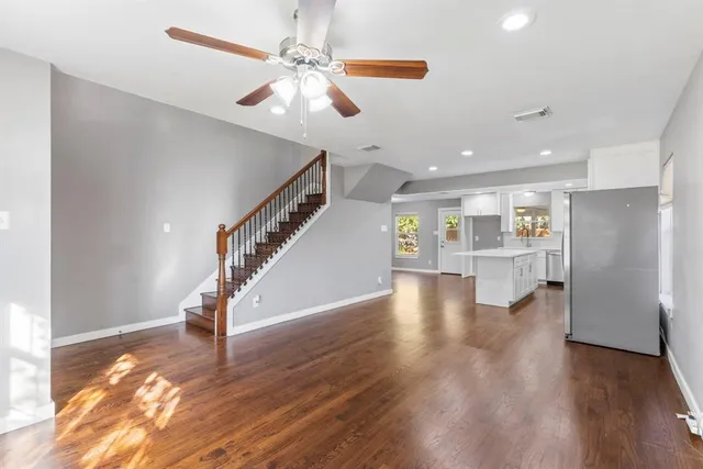 a view of an empty room with wooden floor stairs and a chandelier fan