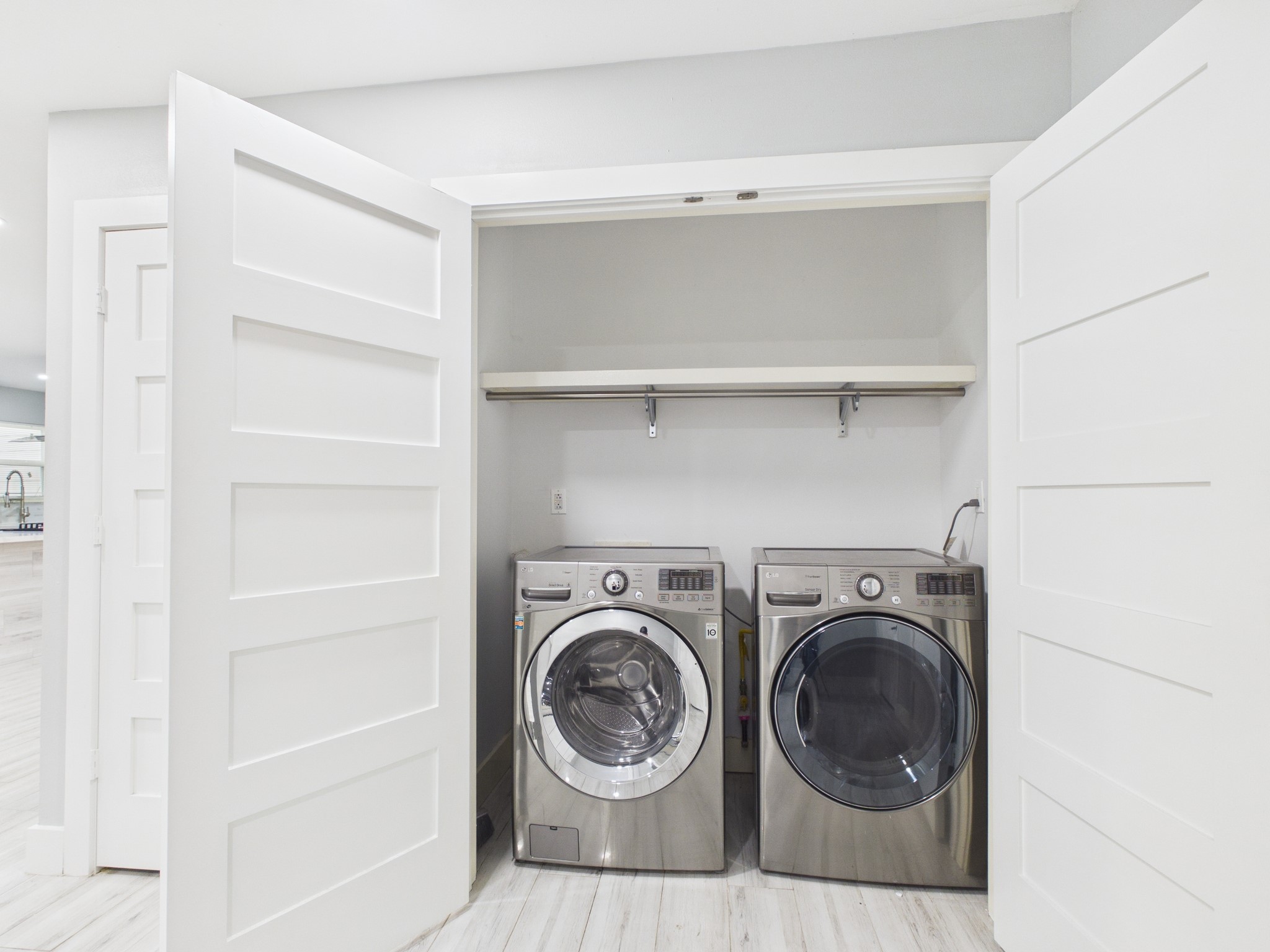 4927 Kelso Street Houston, TX 77021 - Photo 20 of 45 This photo shows a modern laundry area with stainless steel washer and dryer units neatly tucked into a closet with white sliding doors. A shelf above provides extra storage space, and the light-colored flooring and walls create a clean, bright atmosphere.