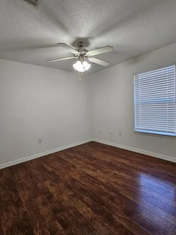 an empty room with wooden floor fan and windows