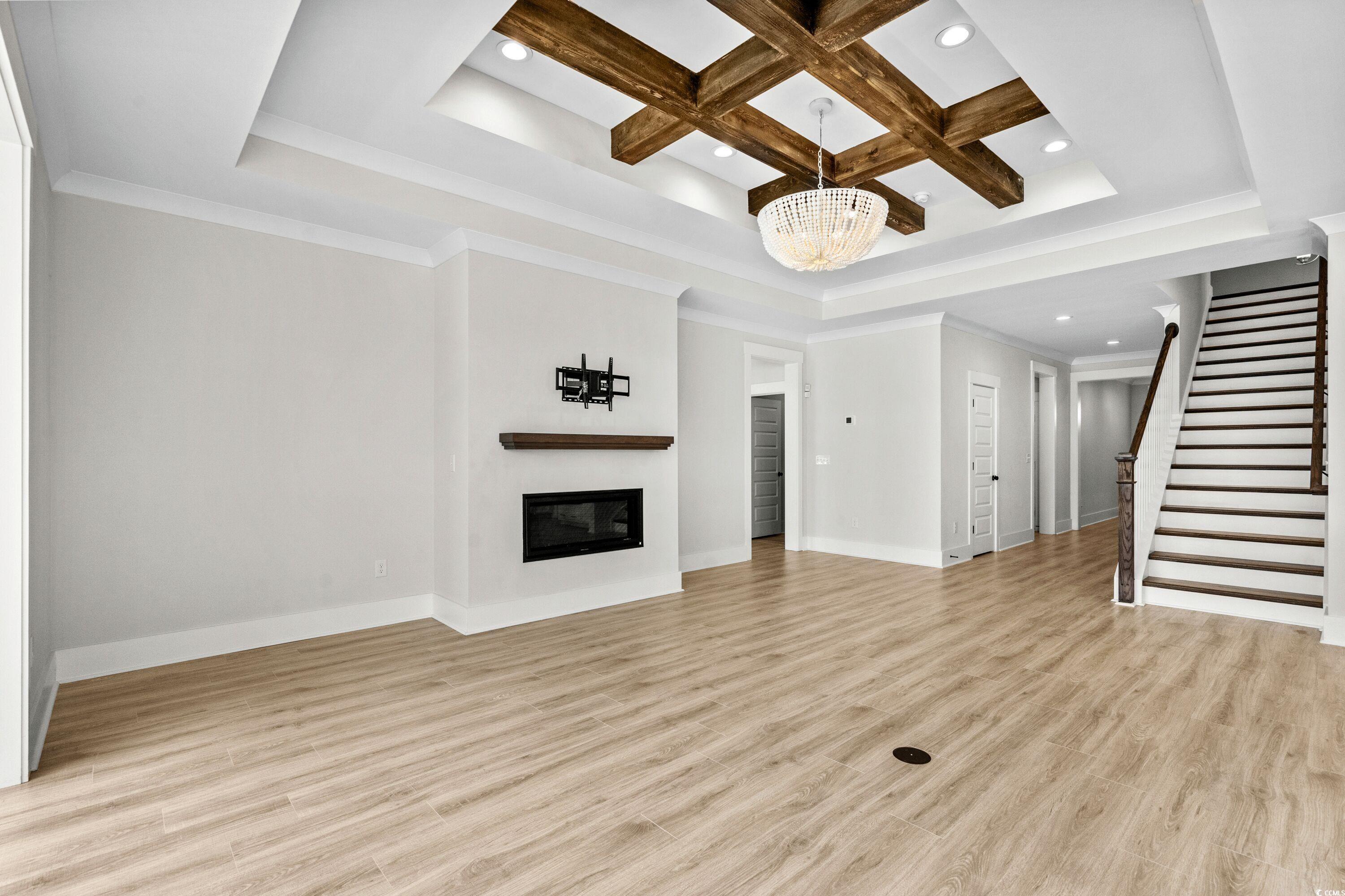9035 Binnicker Drive Murrells Inlet, SC 29576 - Photo 8 of 40 Unfurnished living room featuring a notable chandelier, light wood finished floors, a glass covered fireplace, coffered ceiling, and stairs