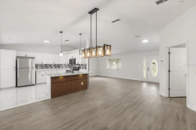 a kitchen with stainless steel appliances granite countertop a refrigerator a sink dishwasher a oven and a dining table with wooden floor