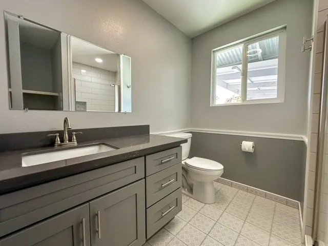 a bathroom with a granite countertop toilet a sink a mirror and a window