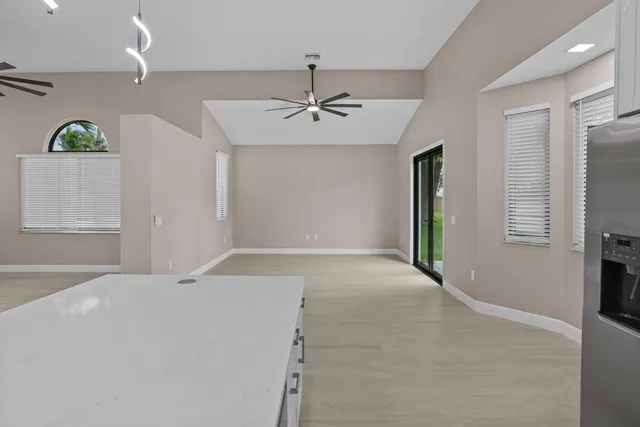 a view of an empty room with window and kitchen view