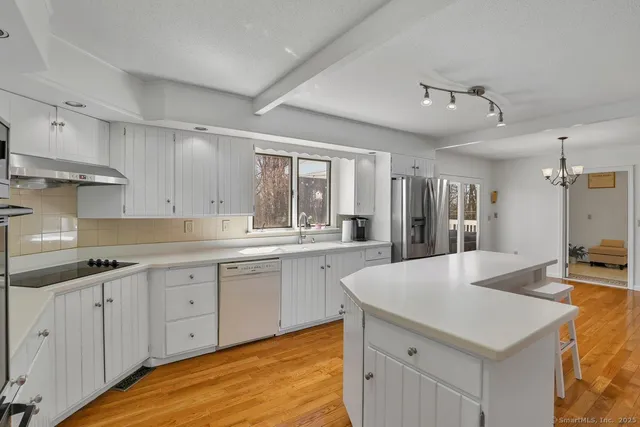 a view of a kitchen with a sink dishwasher a stove and white cabinets with wooden floor