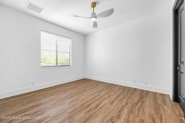 an empty room with wooden floor ceiling fan and windows