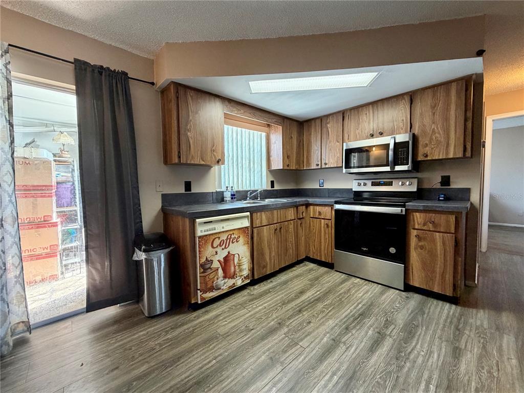 9840 Crofton Lane Port Richey, FL 34668 - Photo 5 of 12 a kitchen with stainless steel appliances granite countertop wooden cabinets a sink a stove a refrigerator with grey cabinets and wooden floor