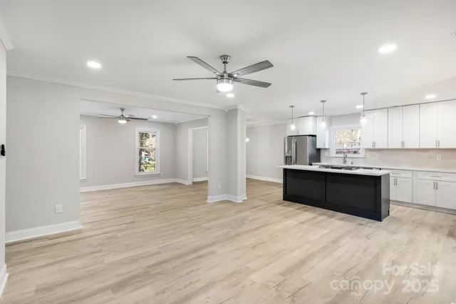 a large white kitchen with kitchen island a sink dishwasher a stove a refrigerator and white cabinets with wooden floor