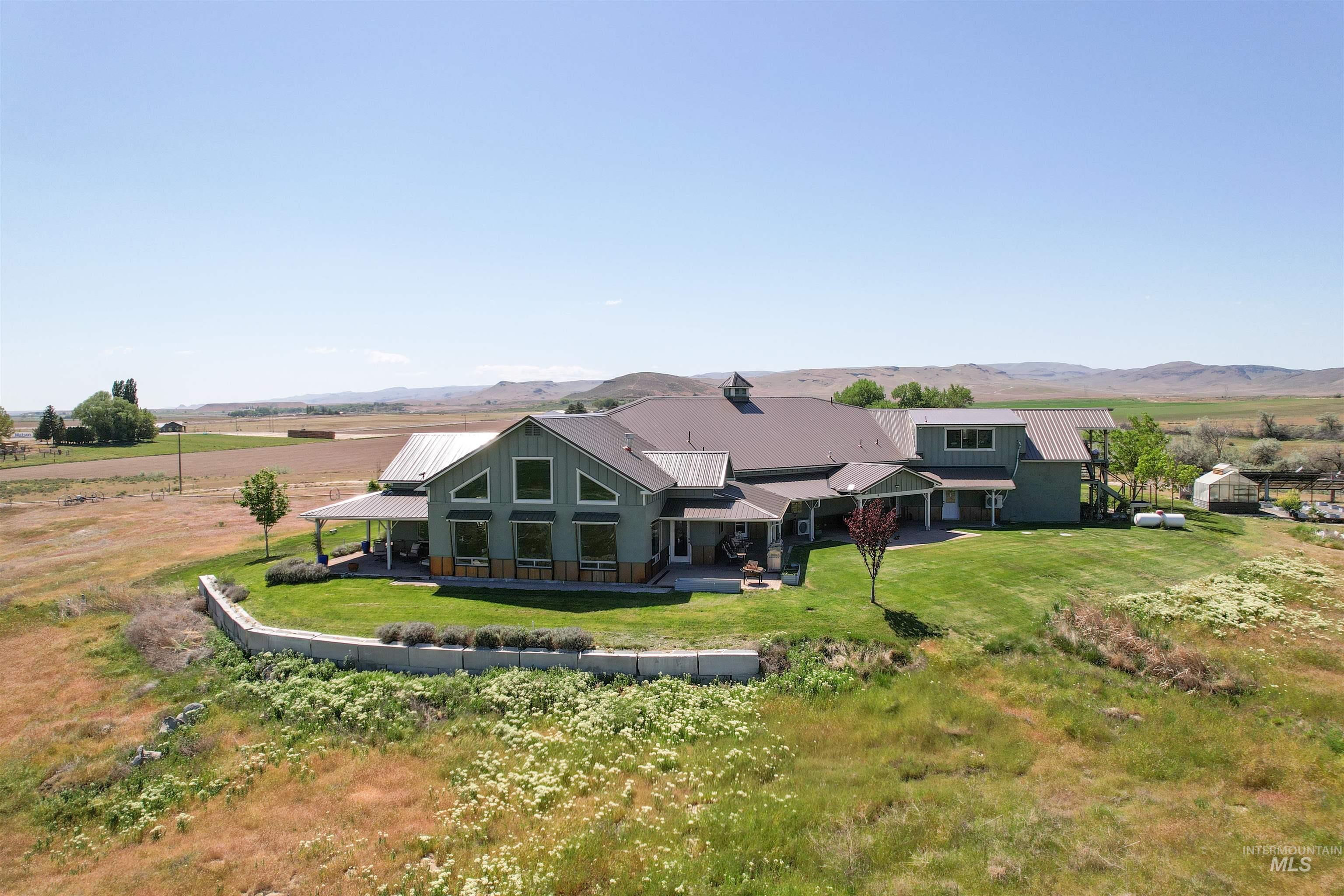 1030 Desert Glen Road Adrian, OR 97901 - Photo 5 of 47 Expansive rural property featuring a sage green exterior with a dark metal roof, multiple covered patios, a manicured lawn, and a retaining wall