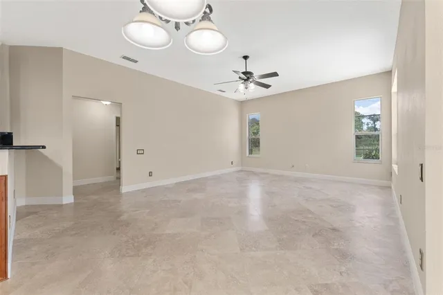 an empty room with a chandelier fan and windows