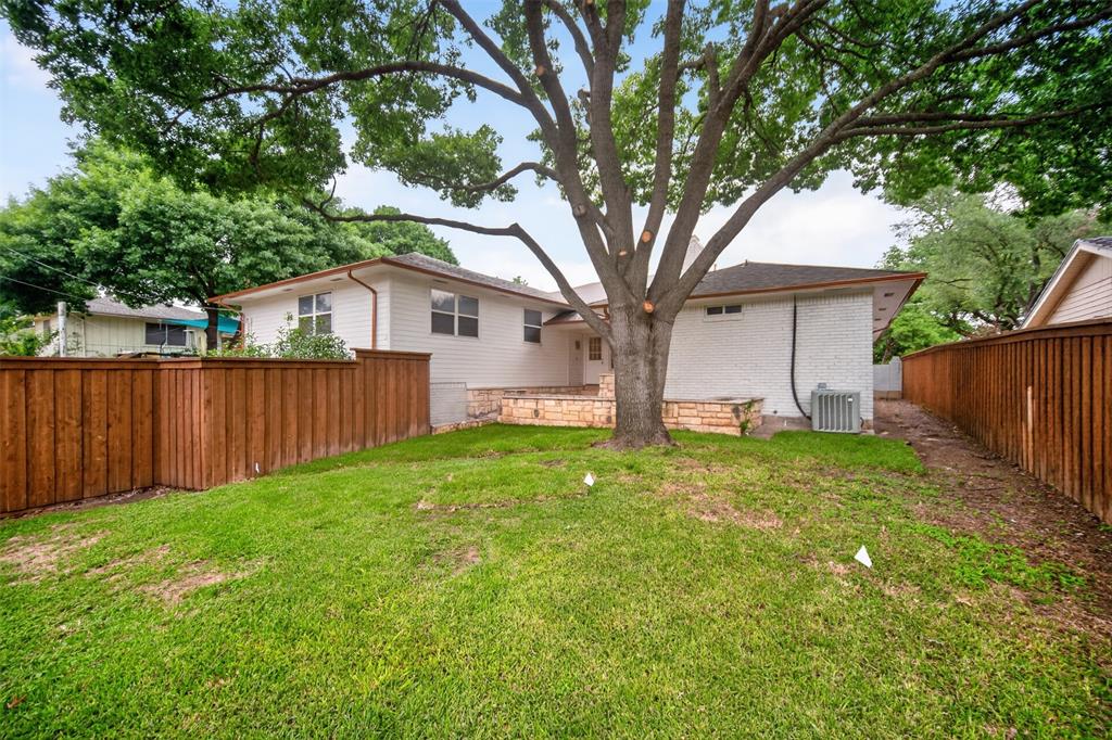 9660 Timberleaf Drive Dallas, TX 75243 - Photo 38 of 40 Expansive backyard with a manicured lawn, featuring a large mature tree, wood privacy fencing, and a white brick exterior with a stone base
