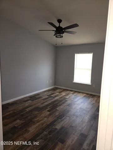 an empty room with wooden floor fan and windows