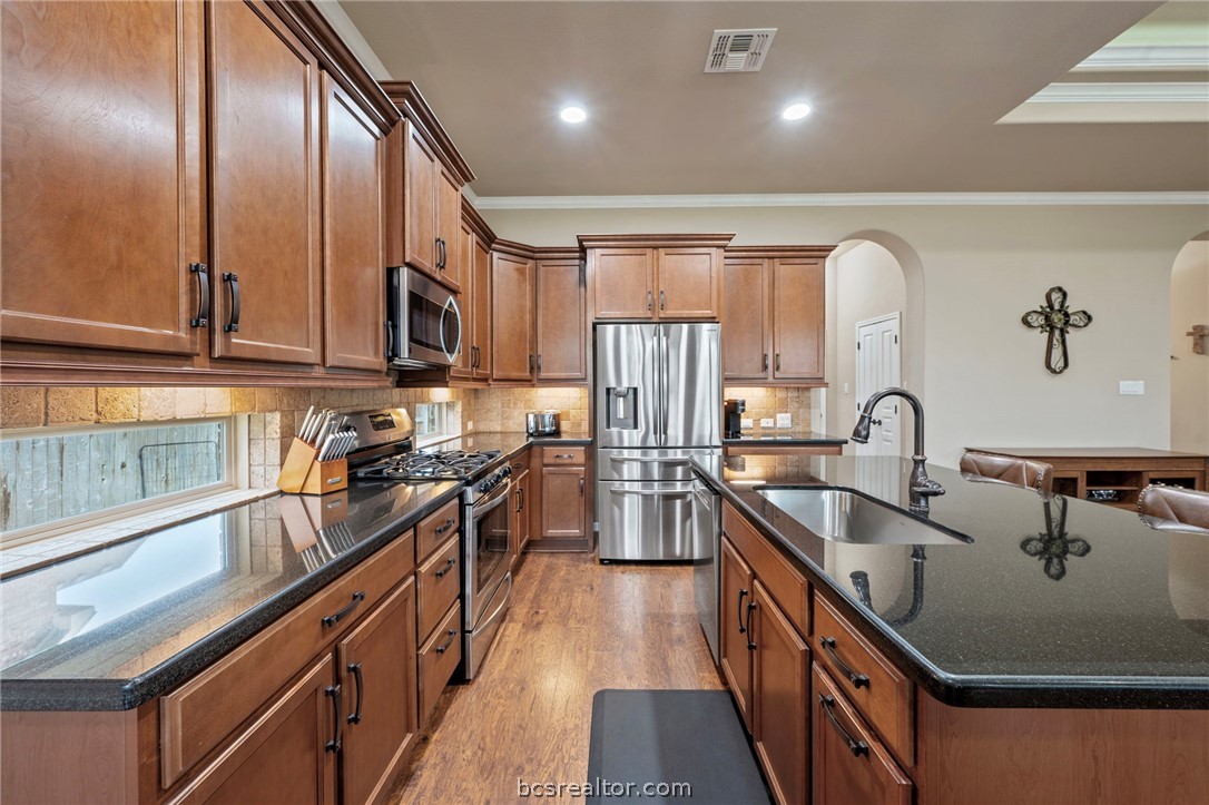 3085 Archer Circle Bryan, TX 77808 - Photo 8 of 32 Kitchen with stainless steel appliances, an island with new stainless sink, dark granite countertops, backsplash, upgraded cabinetry and ornamental molding.