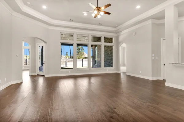 a view of an empty room with wooden floor and a ceiling fan