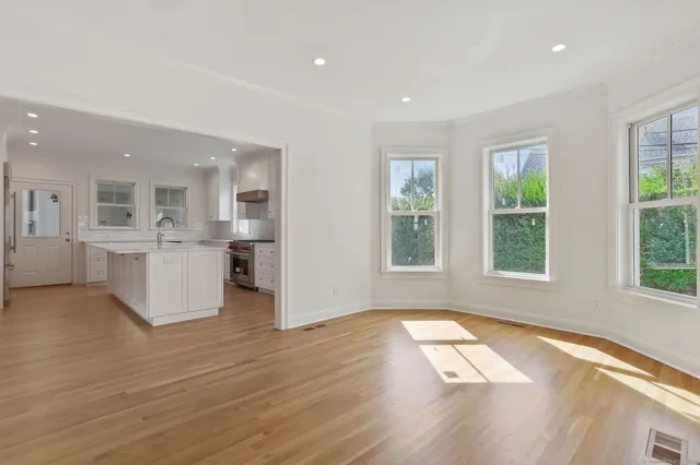 a view of an empty room with wooden floor and a kitchen