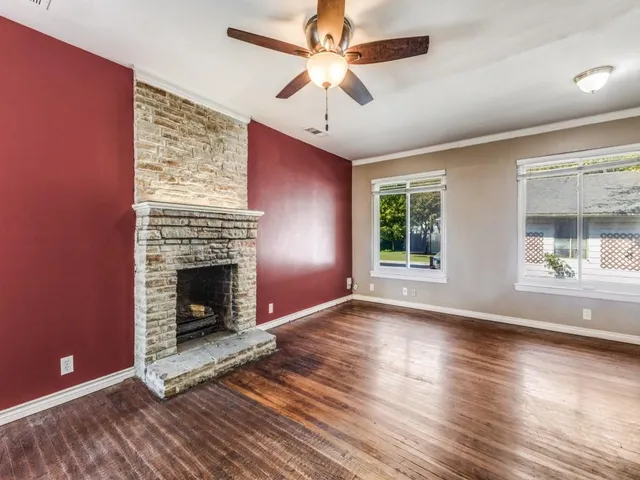 a view of an empty room with wooden floor fireplace and a window