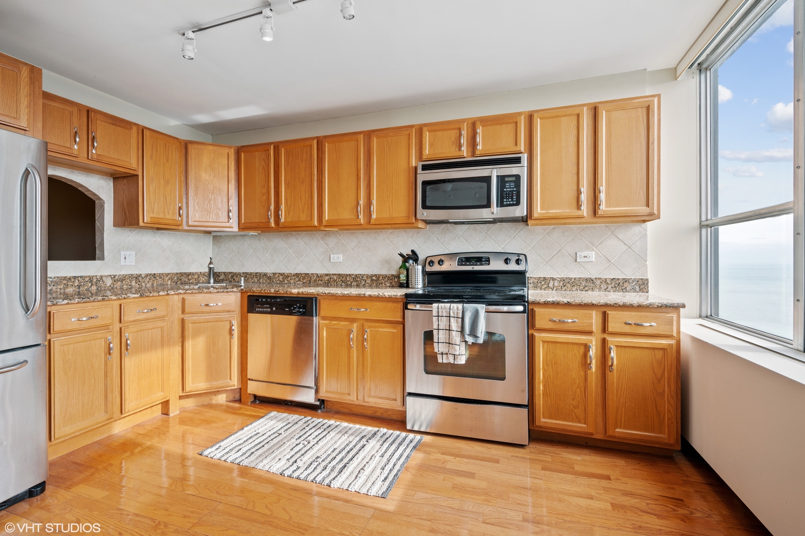 655 West Irving Park Road, Unit 4005 Chicago, IL 60613 - Photo 3 of 12 a kitchen with stainless steel appliances granite countertop a stove top oven a sink dishwasher and a refrigerator with wooden cabinets