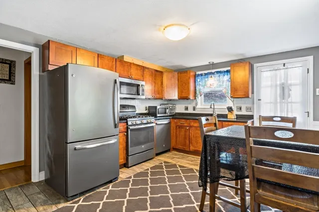 a kitchen with stainless steel appliances granite countertop a refrigerator a stove a sink and a dining table with wooden cabinet